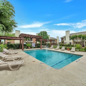 Sparkling swimming pool surrounded by lounge chairs and a poolside pergola at Stonegate Apartments in Mckinney, Texas