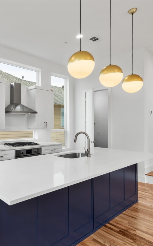 Modern kitchen with white counters and round hanging lights with gold accents at The Collection Townhomes in Dallas, Texas