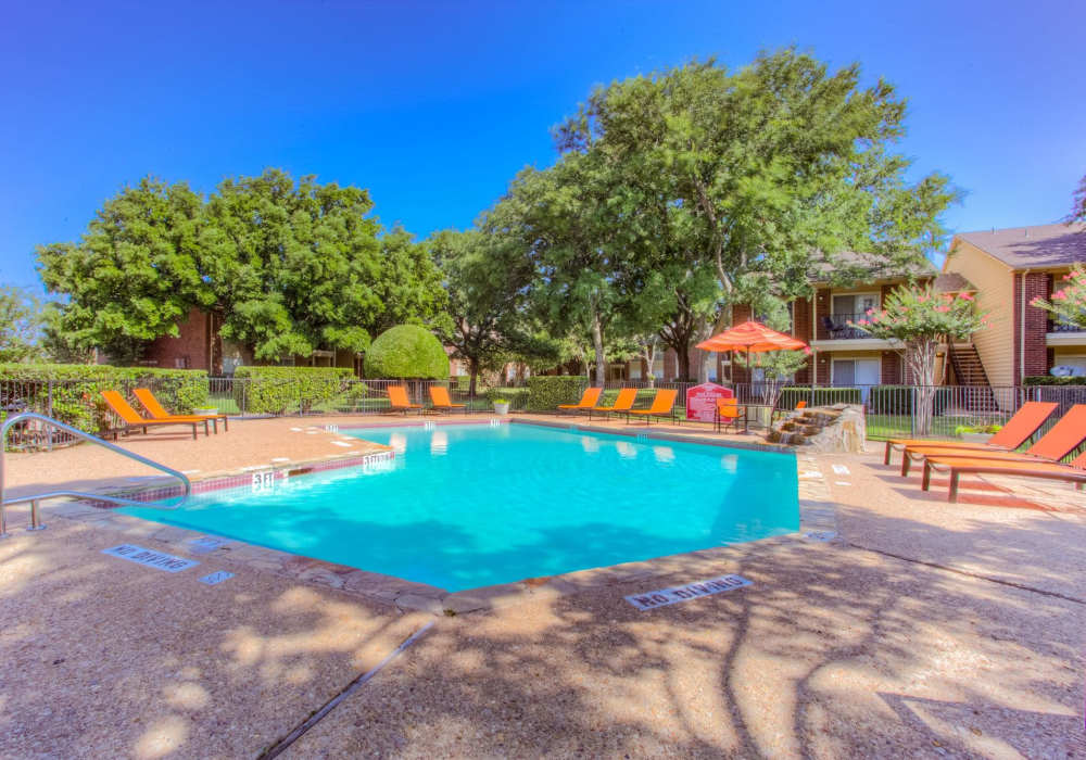 Sparkling water pool surrounded by lush landscaping and vibrant lounge chairs at Charter Oak in Euless, Texas.