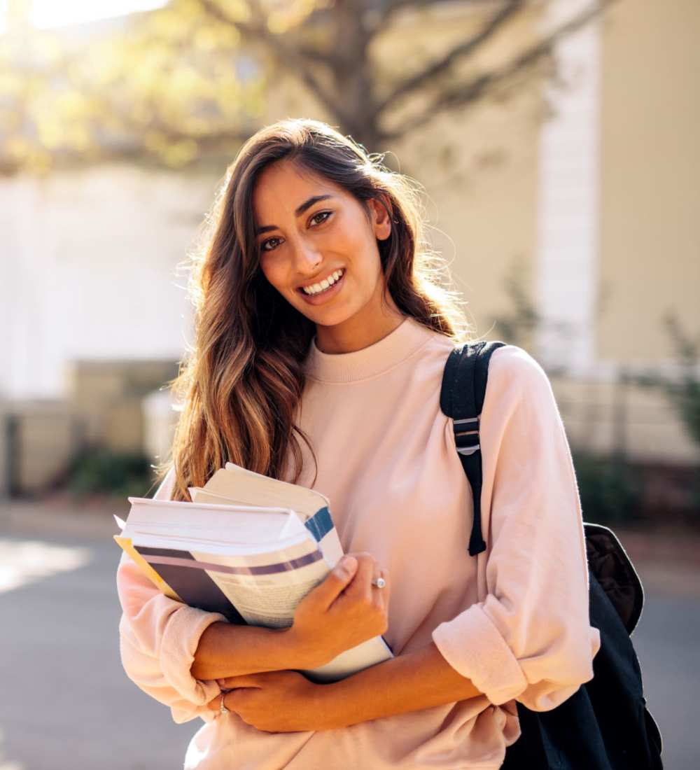 A student smiles between classes while holding her books near Astoria in Denton, Texas