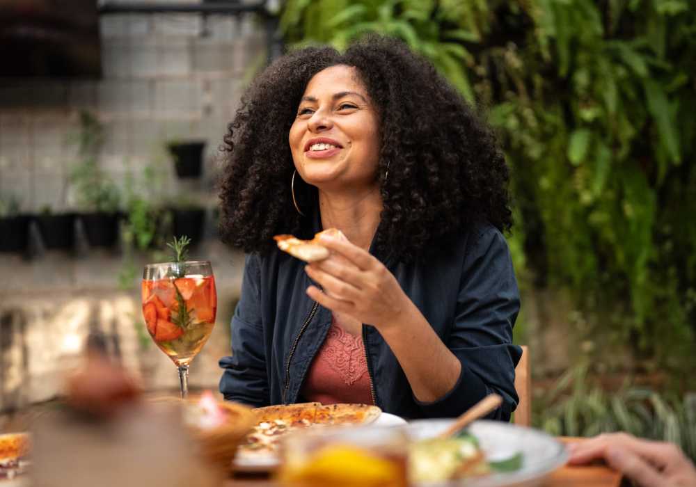 Woman enjoying pizza and drink at outdoor table near Balcones Trails in Kyle, Texas