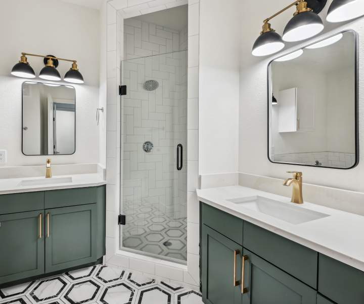 Bright bathroom with vanity lights, mirrors, sinks and glass shower at Dorian and Encore in Plano, Texas