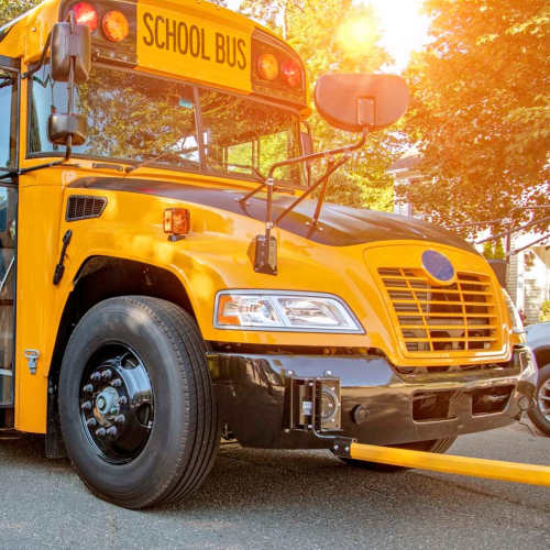 An yellow school bus parked on a tree-lined street with sunlight shining through the leaves at Brea's Crossing Senior Living II in Shelbyville, Kentucky