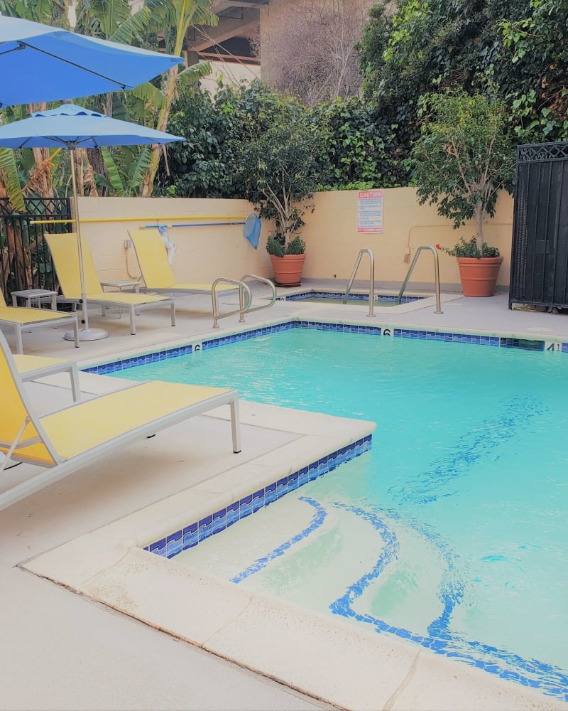 Swimming pool with yellow lounge chairs and blue umbrellas at Ariel Court, Los Angeles, California