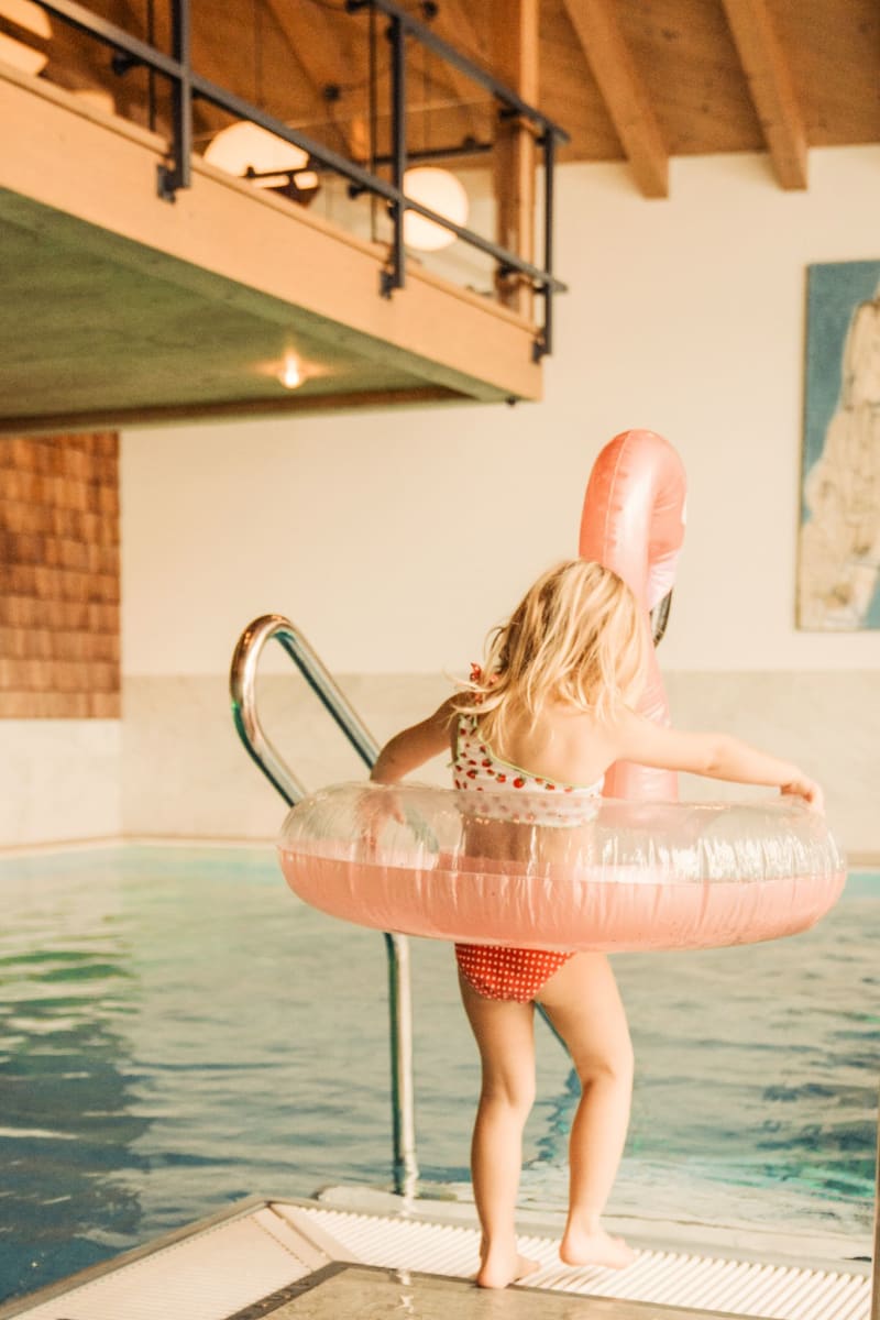 Ein kleines Mädchen mit einem Schwimmreifen steht am Pool im Glemmtalerhof in Hinterglemm.
