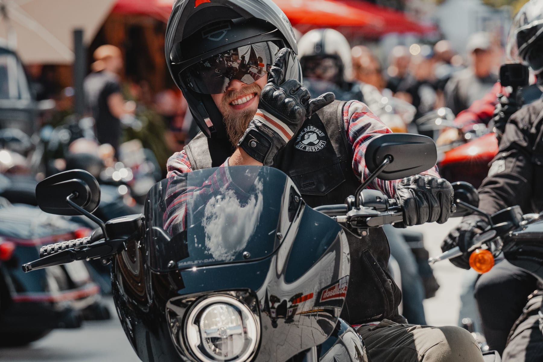 Motorradfahrer winkt in Hinterglemm, umgeben von anderen Motorrädern und fröhlicher Atmosphäre.