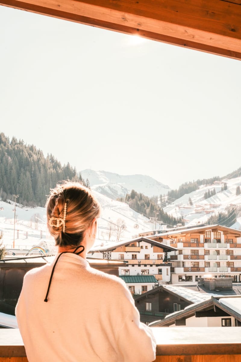 Eine Person blickt auf die schneebedeckten Berge und den Glemmtalerhof in Hinterglemm.