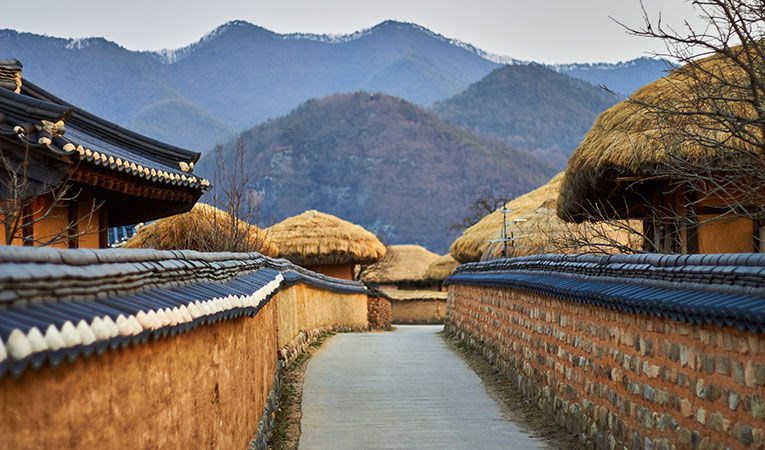 Looking down a walled path with straw roofs and mountains in Andong, South Korea