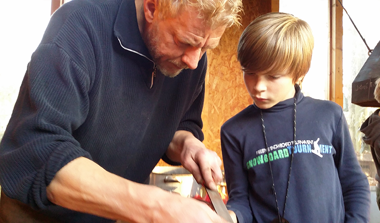 old man showing a young boy how to use a tool