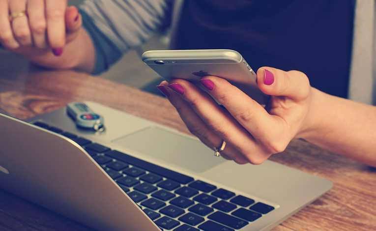 Womans hands holding phone with open laptop