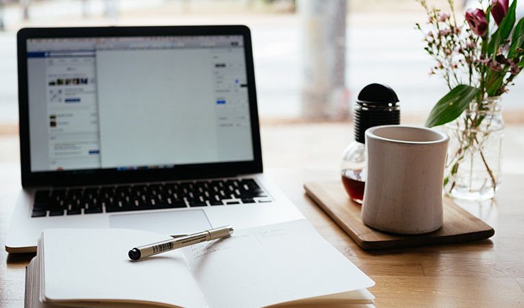 how to get tefl certification online. Open laptop and notebook with a cup of coffee.