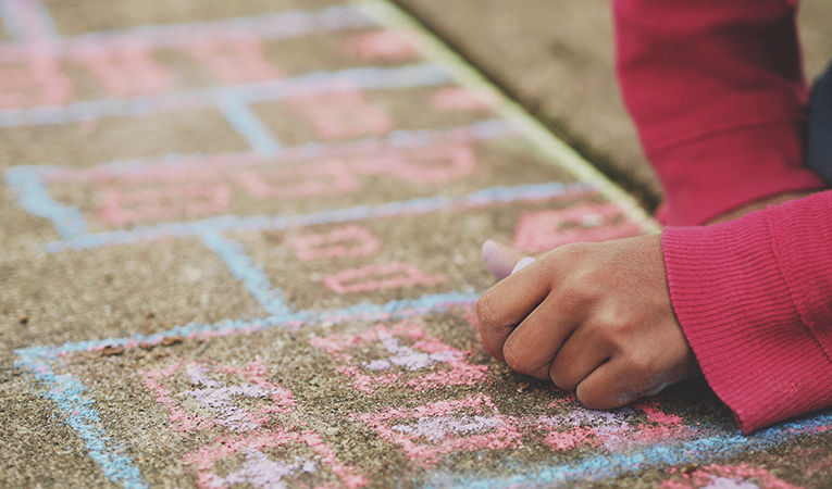 how to get tefl certification online. Close up of girl in pink sweater drawing with chalk on sidewalk.