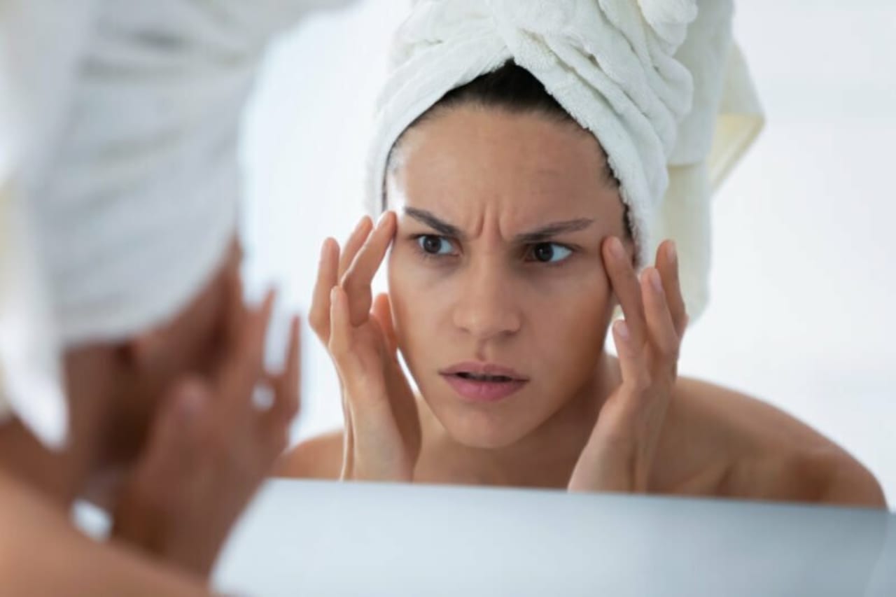 Woman pulls and frowns at wrinkles on skin in mirror