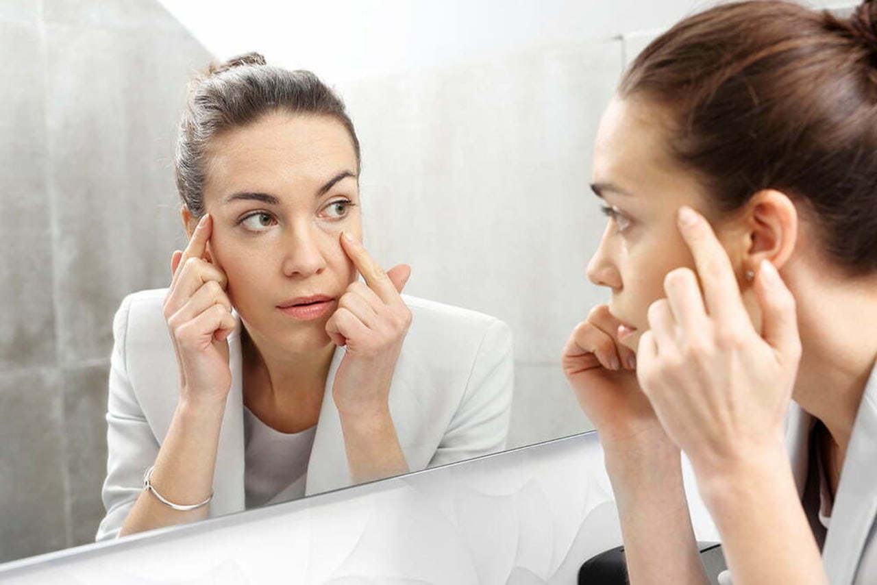 Woman looking in mirror examining upper and lower eyelids