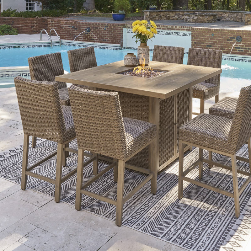 An outdoor patio furniture set with six matching chairs around a square pub height table with a fire feature in its middle.