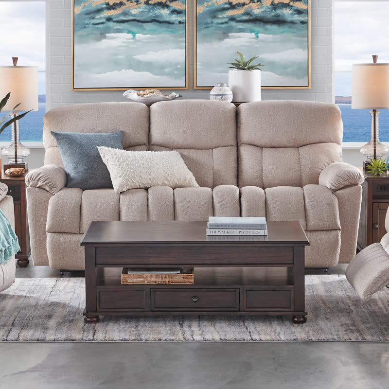 An ivory reclining sofa with gray and white throw pillows and a dark brown wooden coffee table in a living room.