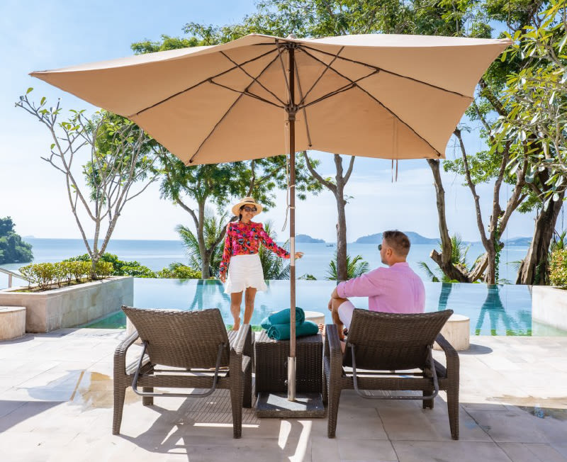 A man and a woman sitting on patio chairs overlooking water in a tropical paradise.