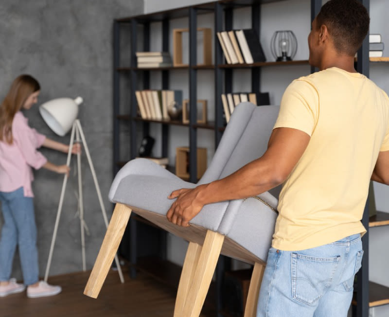 A man and a woman are moving a chair and a floor lamp into place in a living room.