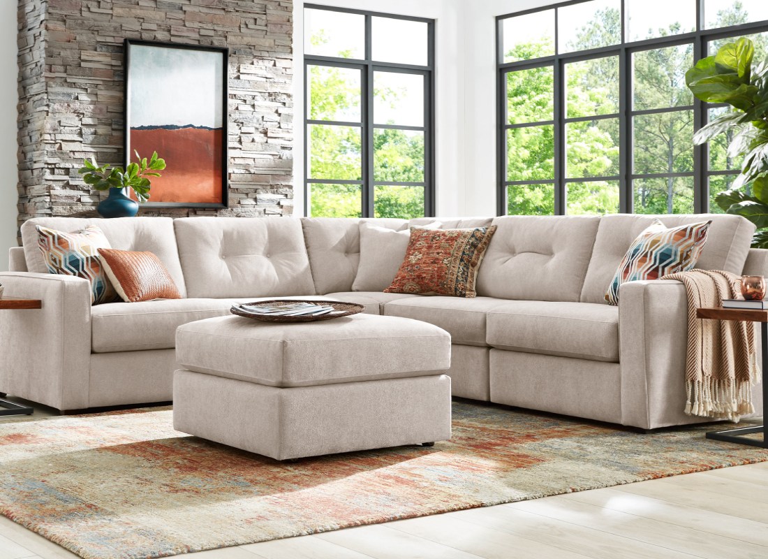 Light tan L-shaped sectional couch with matching square ottoman in a living room.