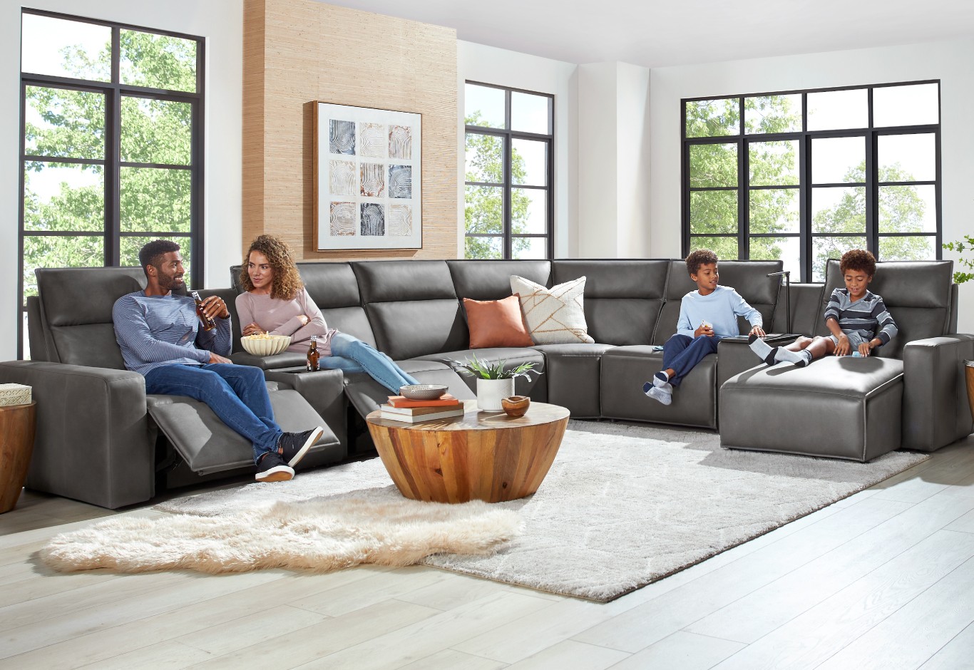 A gray colored L-shaped modular sectional sofa with a family of four sitting on it using the reclining features.
