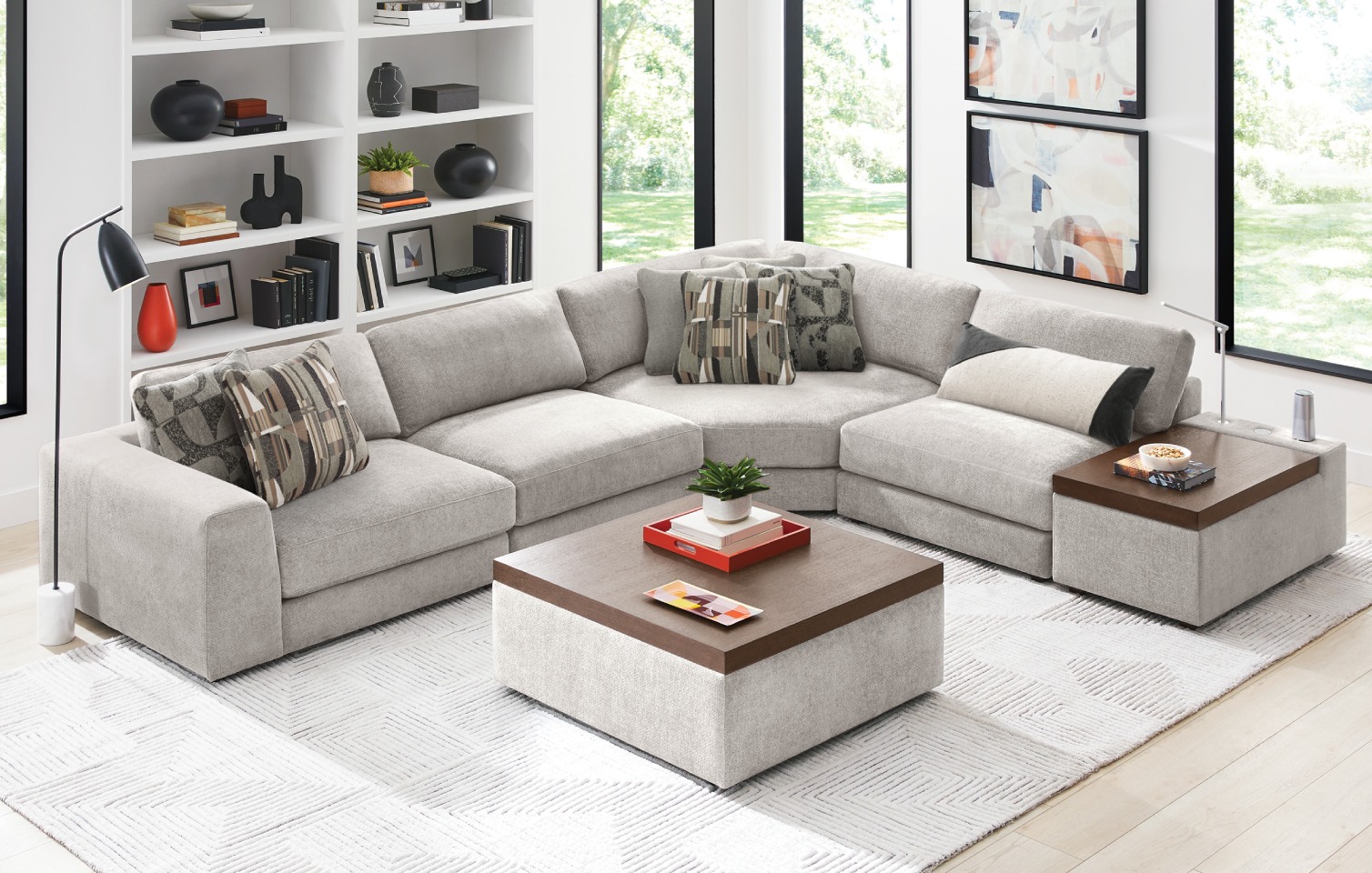 An L-shaped modular sectional couch in light gray upholstery with a matching console and ottoman. The ottoman and console have dark brown wooden tops.