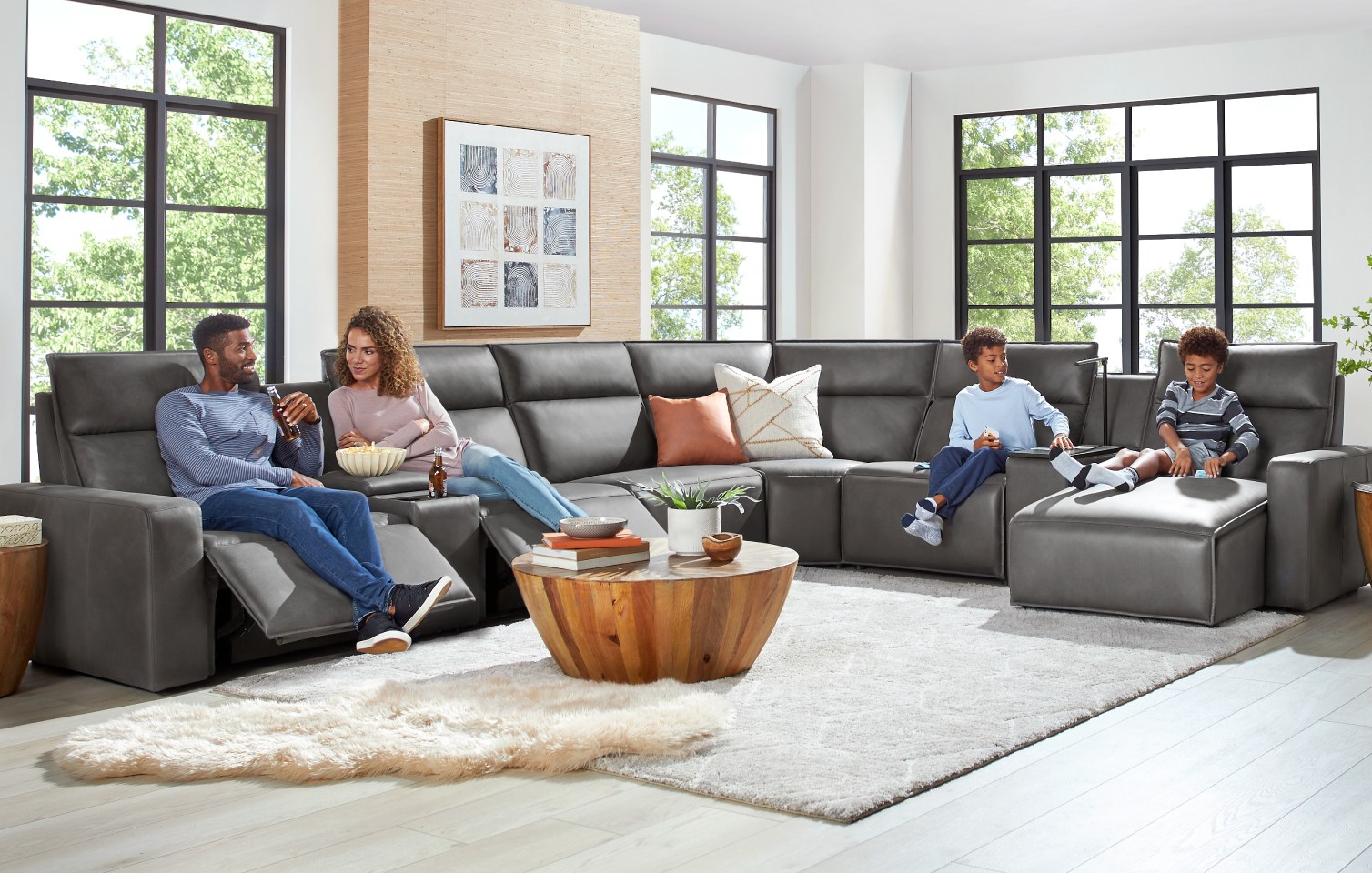 An L-shaped modular sectional couch in light gray upholstery with a matching console and ottoman. The ottoman and console have dark brown wooden tops.