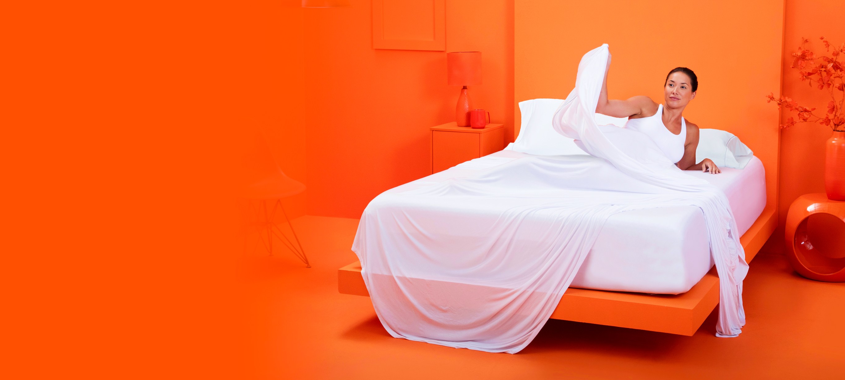 Woman relaxing on a bed with sheets and pillows inside an orange room.