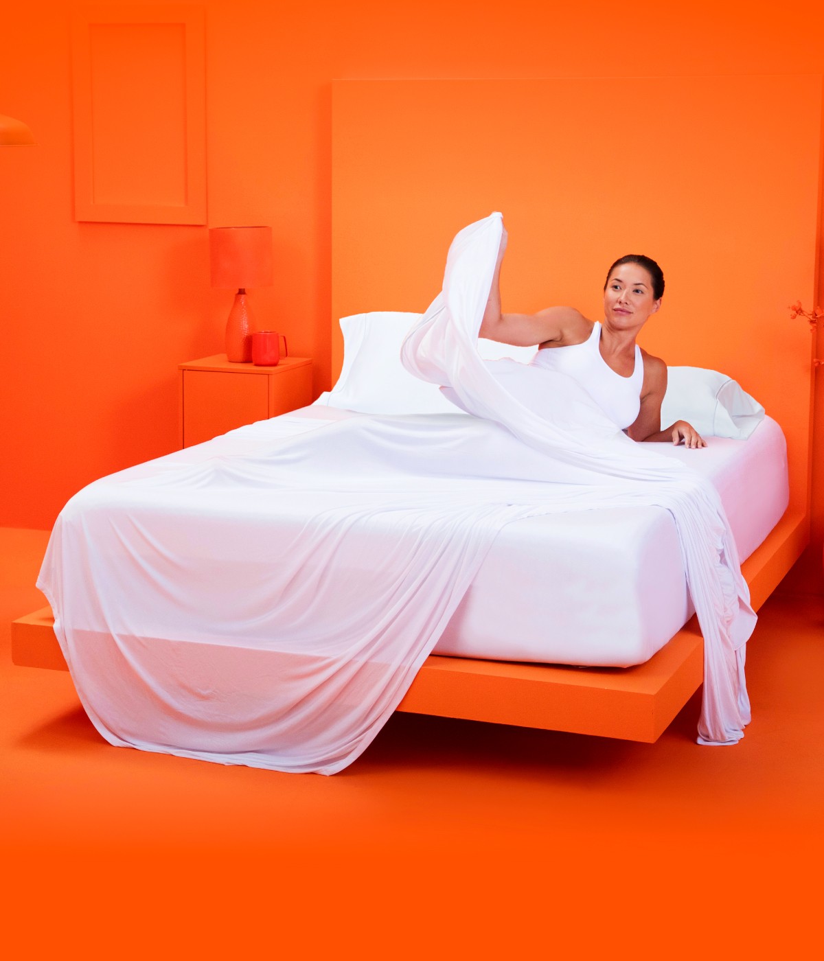 Woman relaxing on a bed with sheets and pillows inside an orange room.