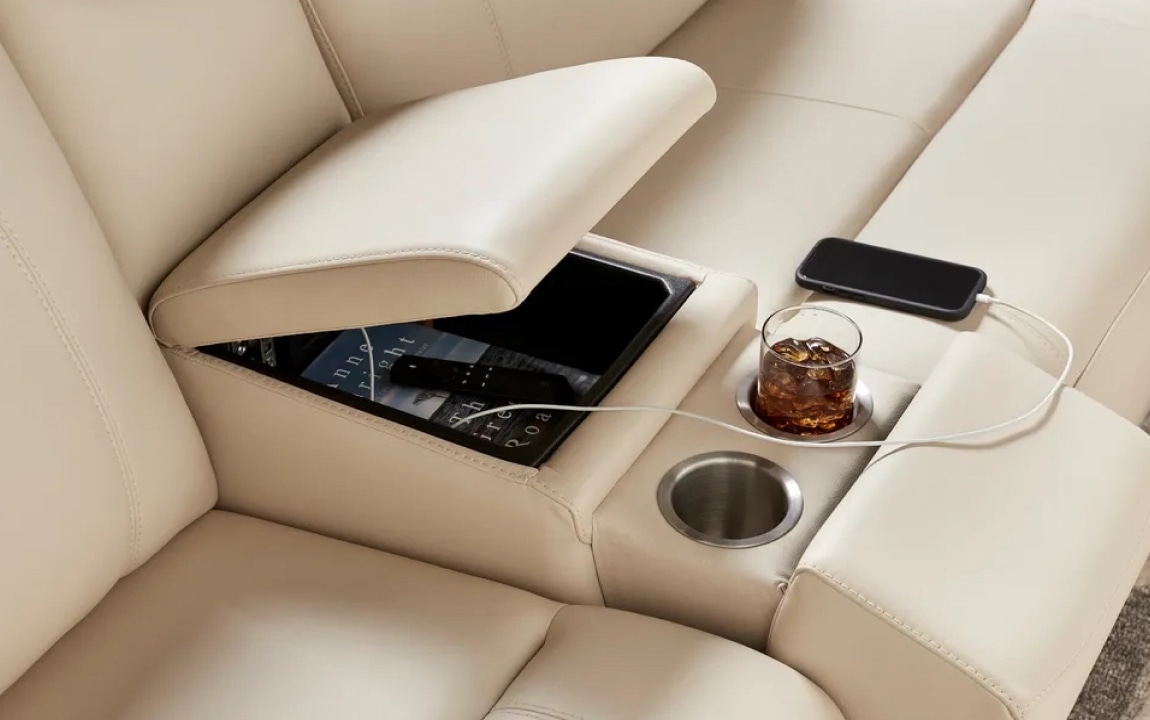 A close up of an ivory colored leather console with a storage console, USB charging ports, and cupholders.