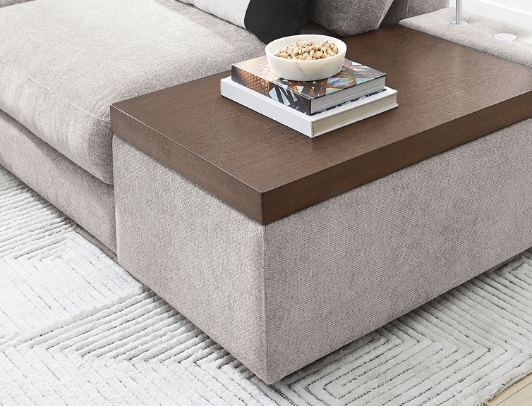A light gray upholstered console with a moveable brown wooden top that acts as a table.