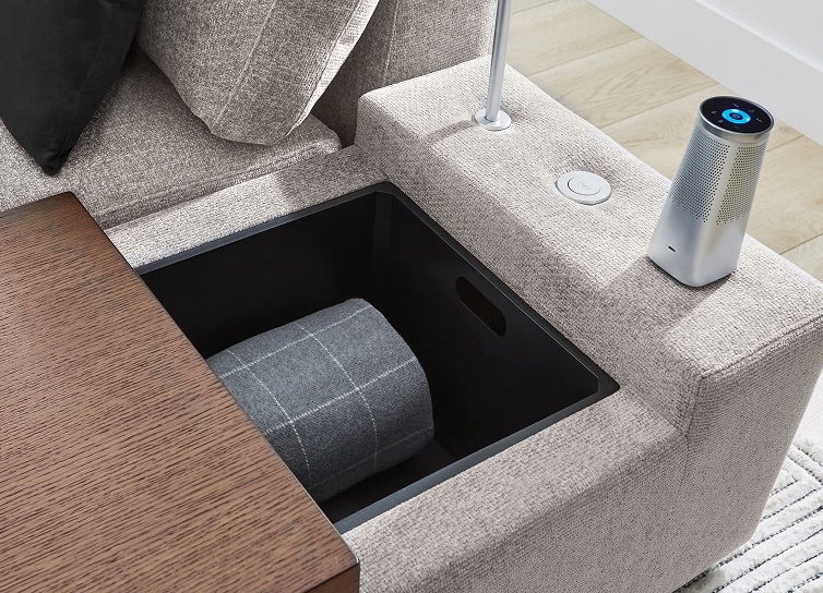 A close up image of a light gray upholstered console with hidden storage and a plug in light.