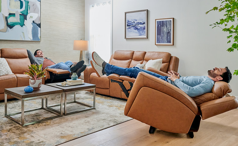 Drew & Jonathan Scott reclining on light brown leather living room furniture including a recliner, a loveseat, and a sofa.