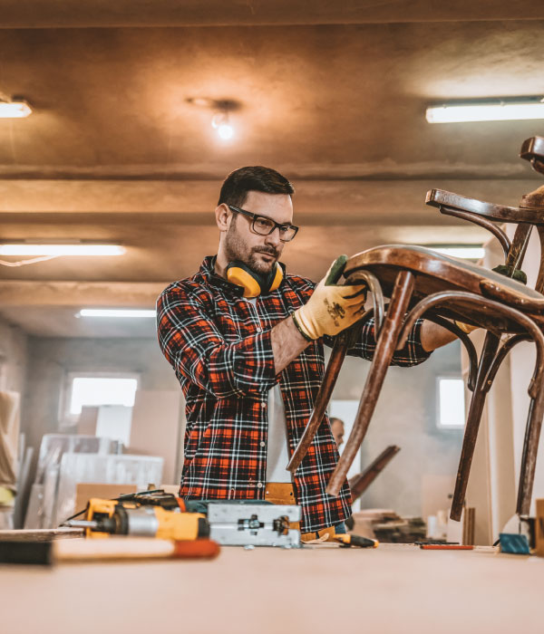 Man inspecting a wooden chair in a workshop.
