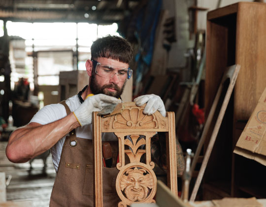 Man in a workshop repairing a wooden chair.