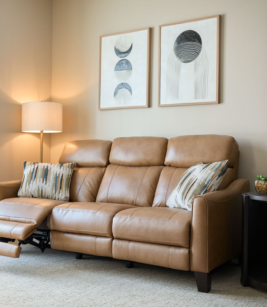 A warm living room with a tan leather reclining sofa and framed wall art