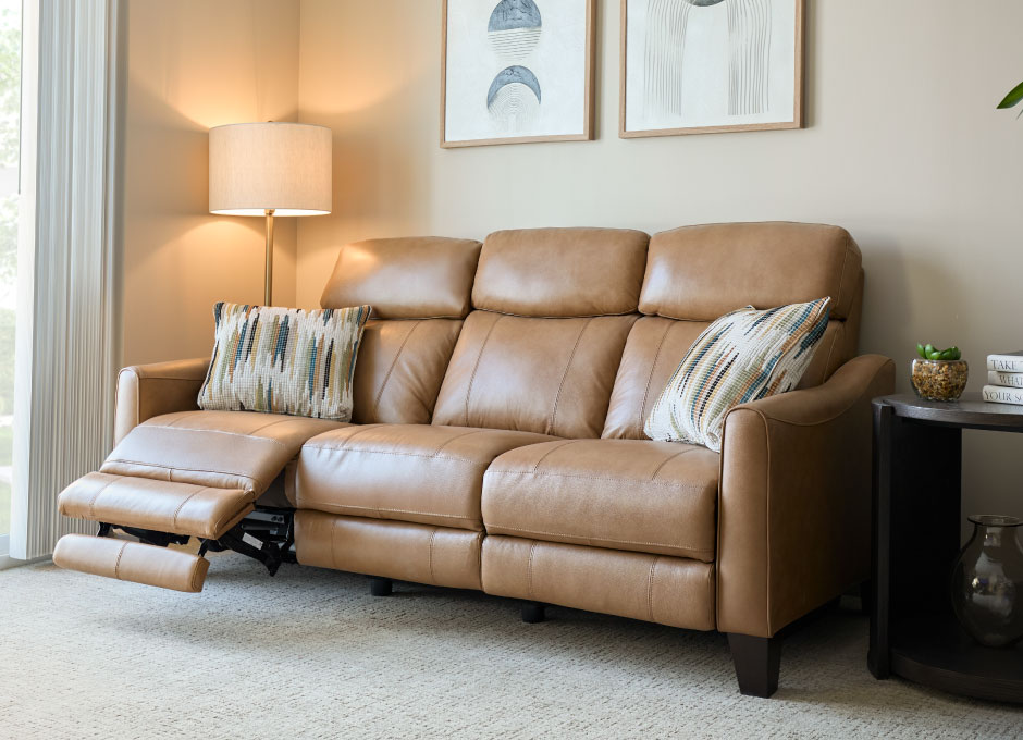A warm living room with a tan leather reclining sofa and framed wall art