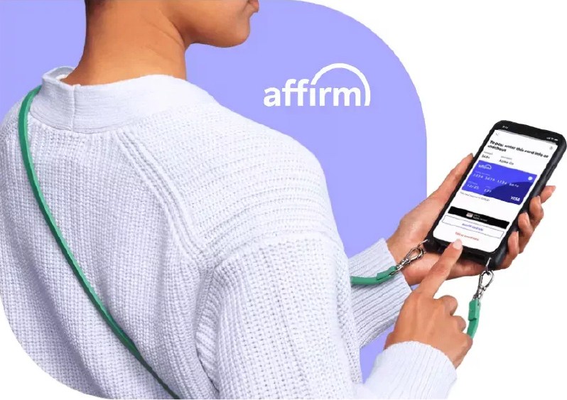 A picture of a woman wearing a white sweater while she's online on her cellular phone applying for Affirm financing.