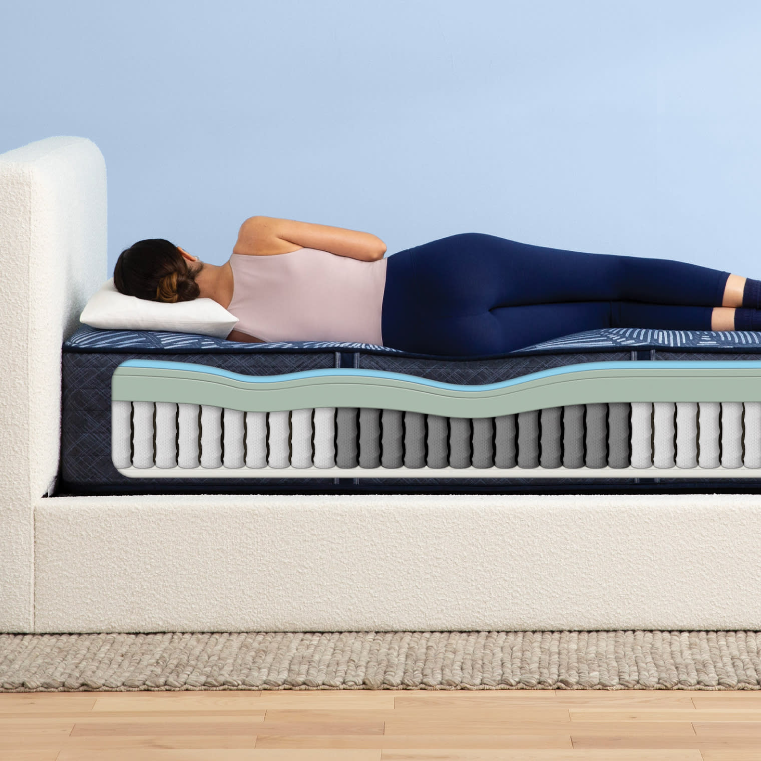 A side view of a hybrid mattress with a woman laying atop it on her side. There is a cutaway showing the layers of materials within the mattress.