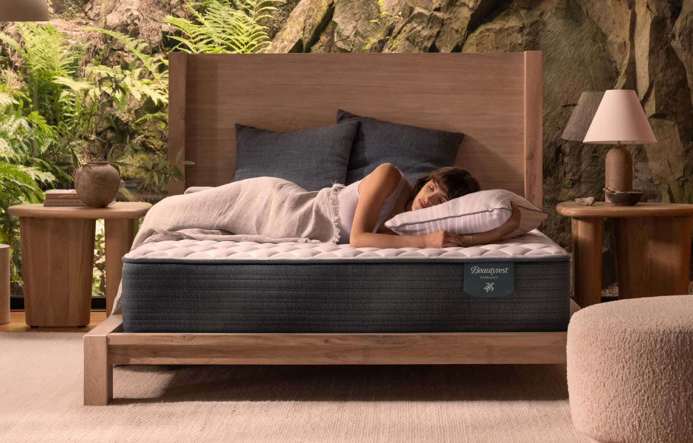 A woman laying on her side atop a Beautyrest queen sized bed in a bedroom with house plants.