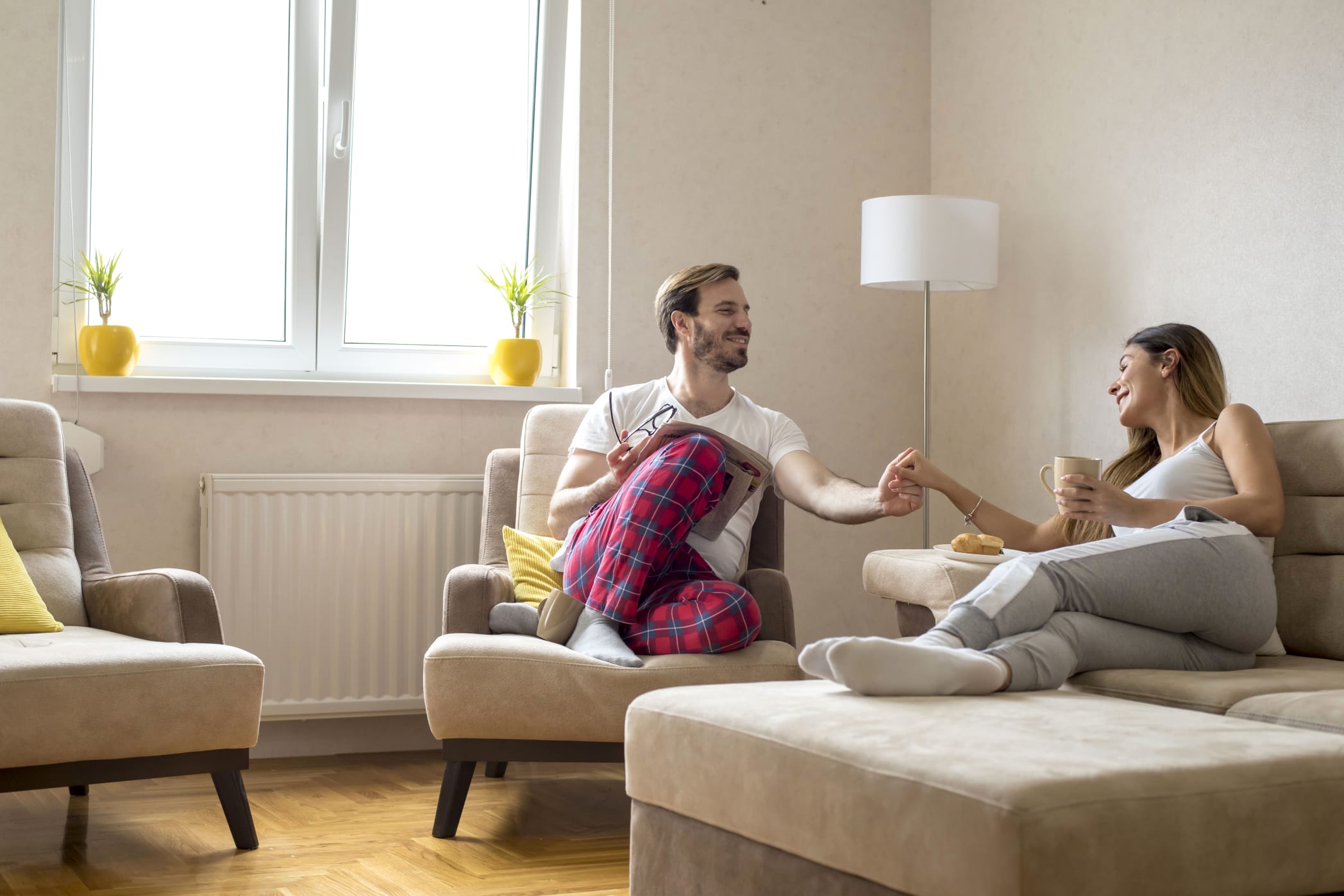 A couple holding hands sitting on their living room furniture.