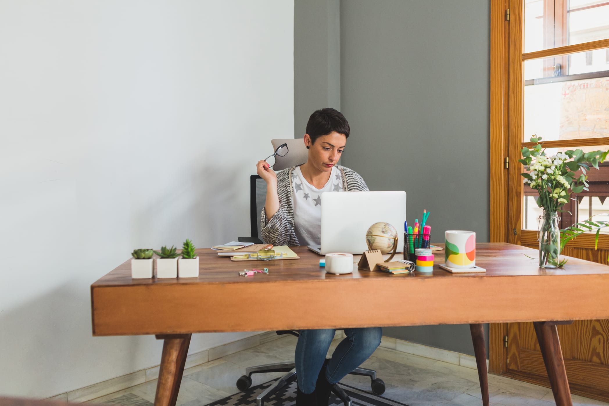 A woman sits at her home office desk reviewing a paper