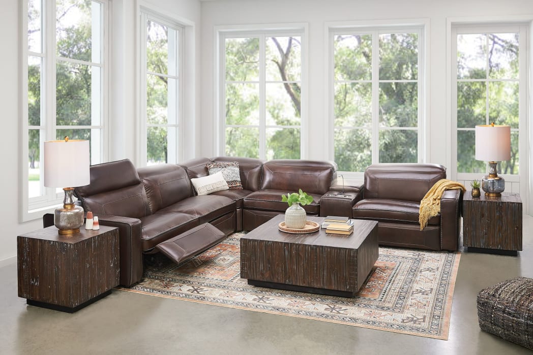 A medium brown leather power reclining sectional couch with solid wood end tables and matching coffee table