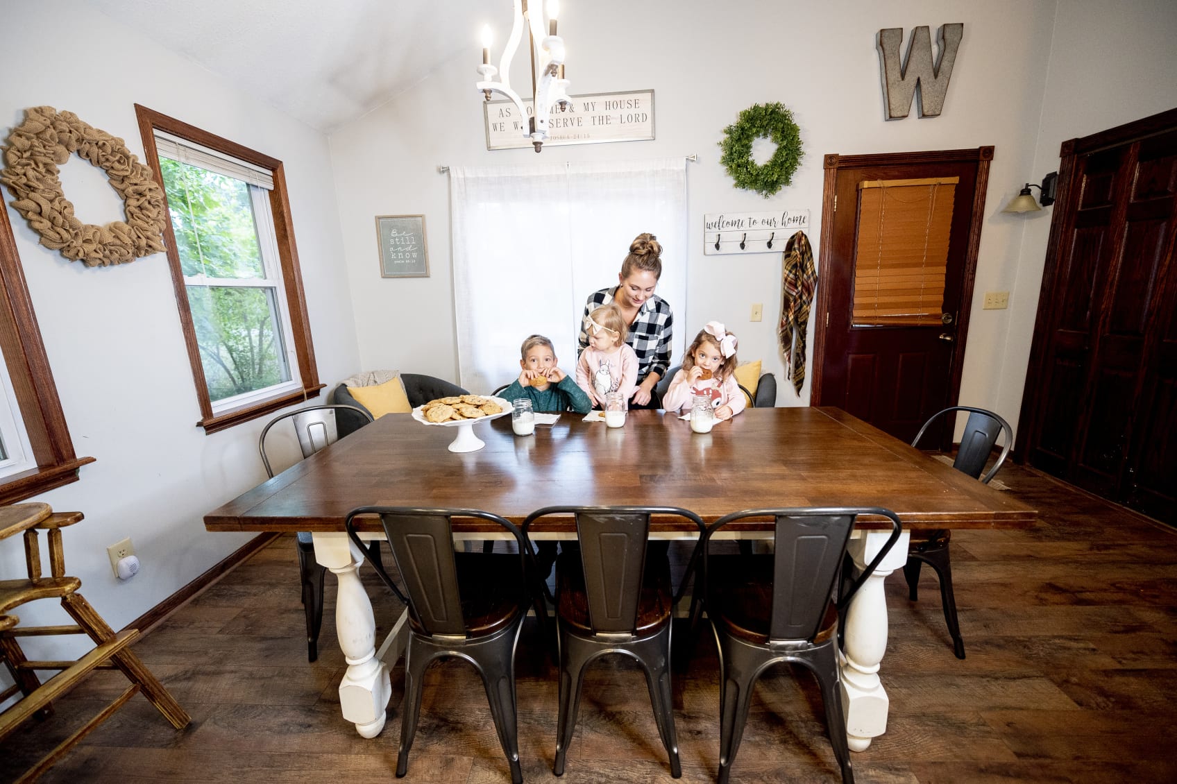 A mom and three kids share cookies and milk at the dining room table.