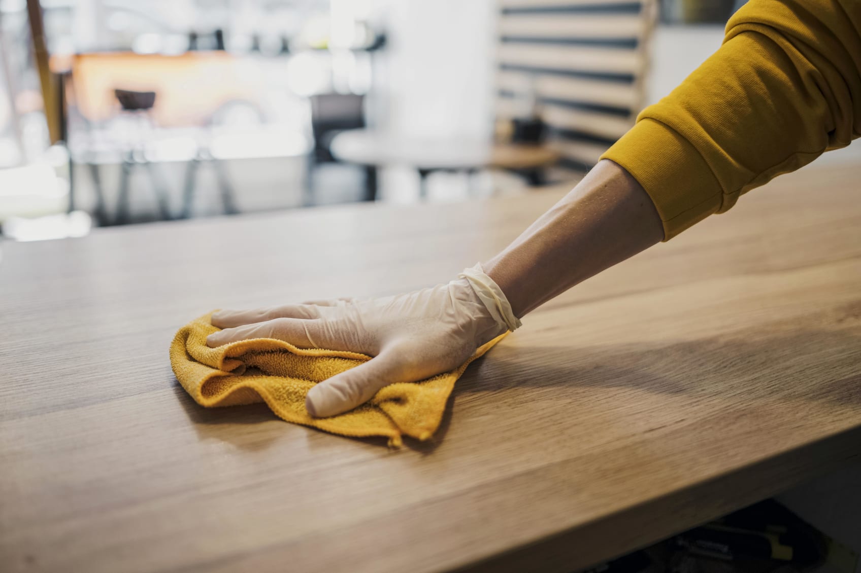 A gloved hand wipes down a wood table with a rag