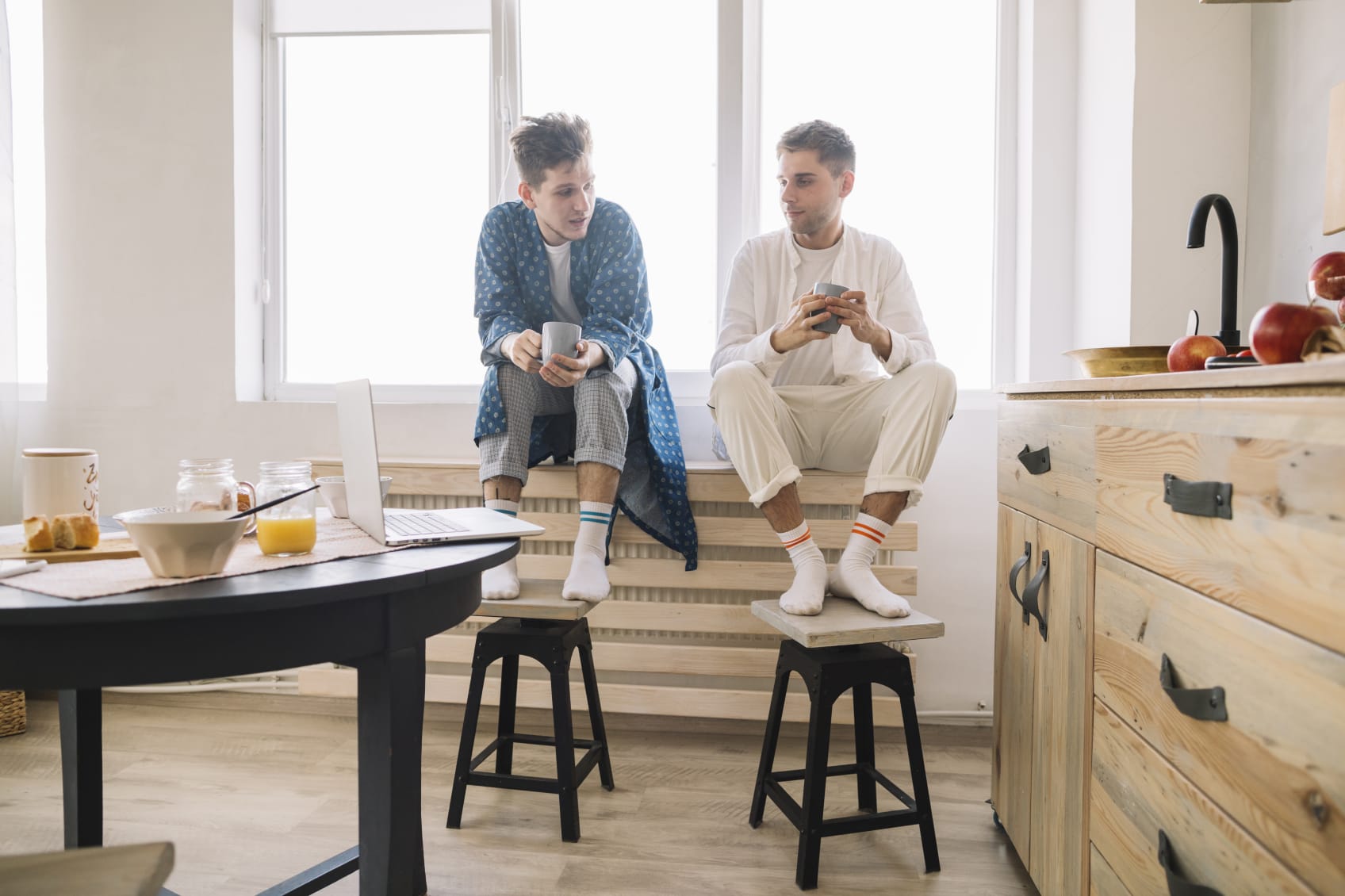 Two men sitting on top of a radiator with their feet on bar stools drinking coffee