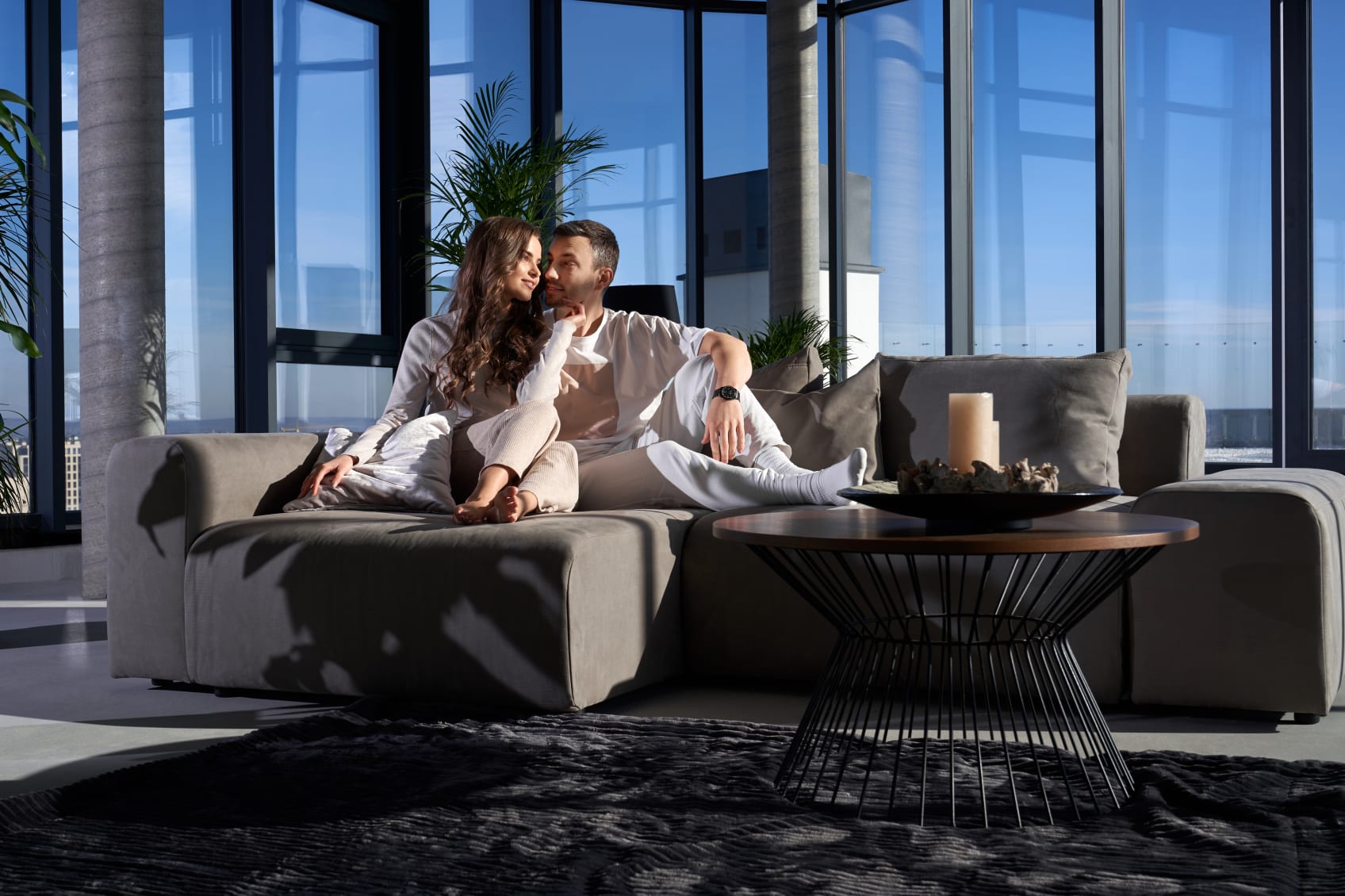 A man and a woman sitting together on a dark gray sectional sofa