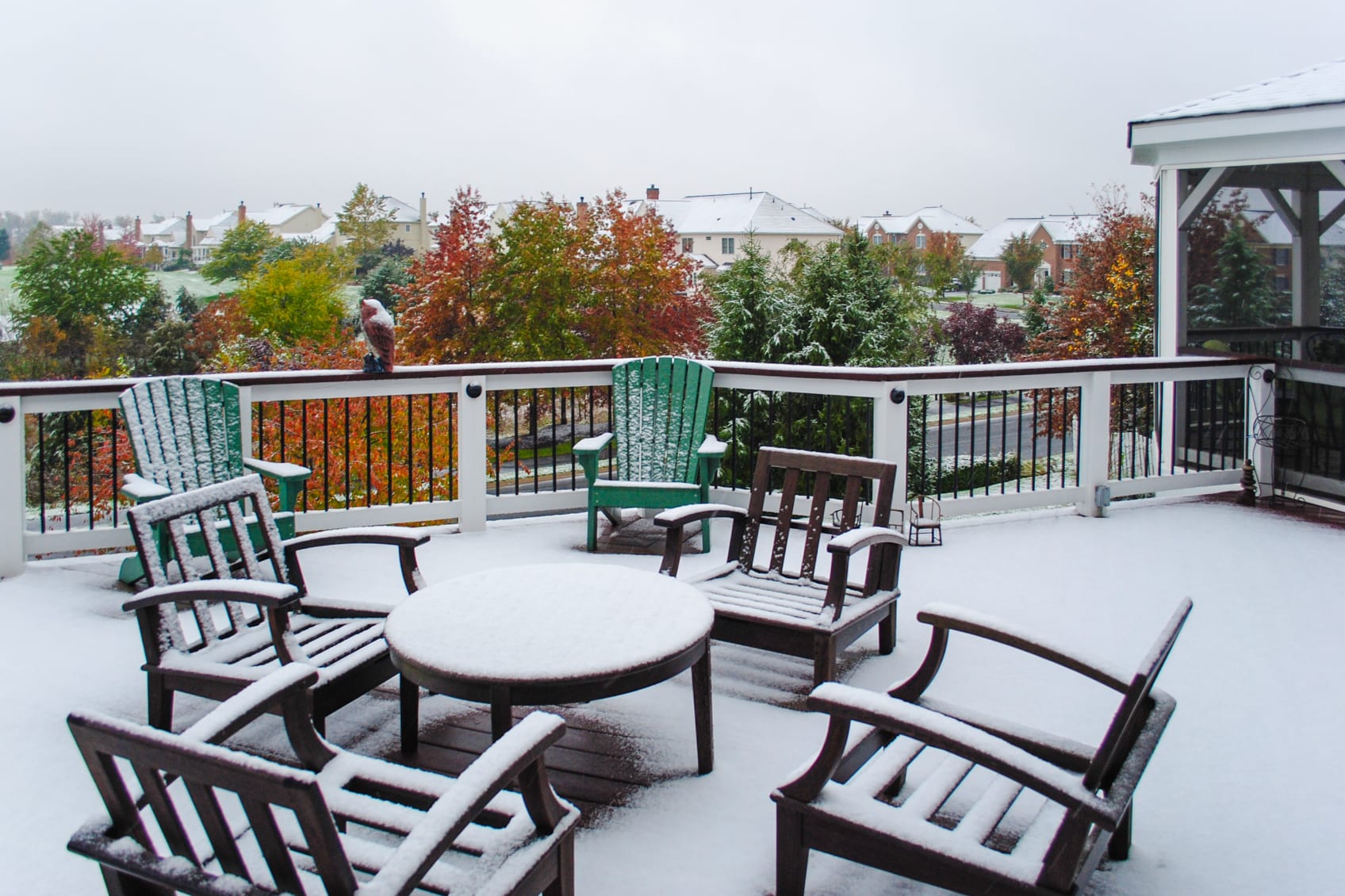 Six outdoor chairs and a tables coated in snow in a suburban backyard.