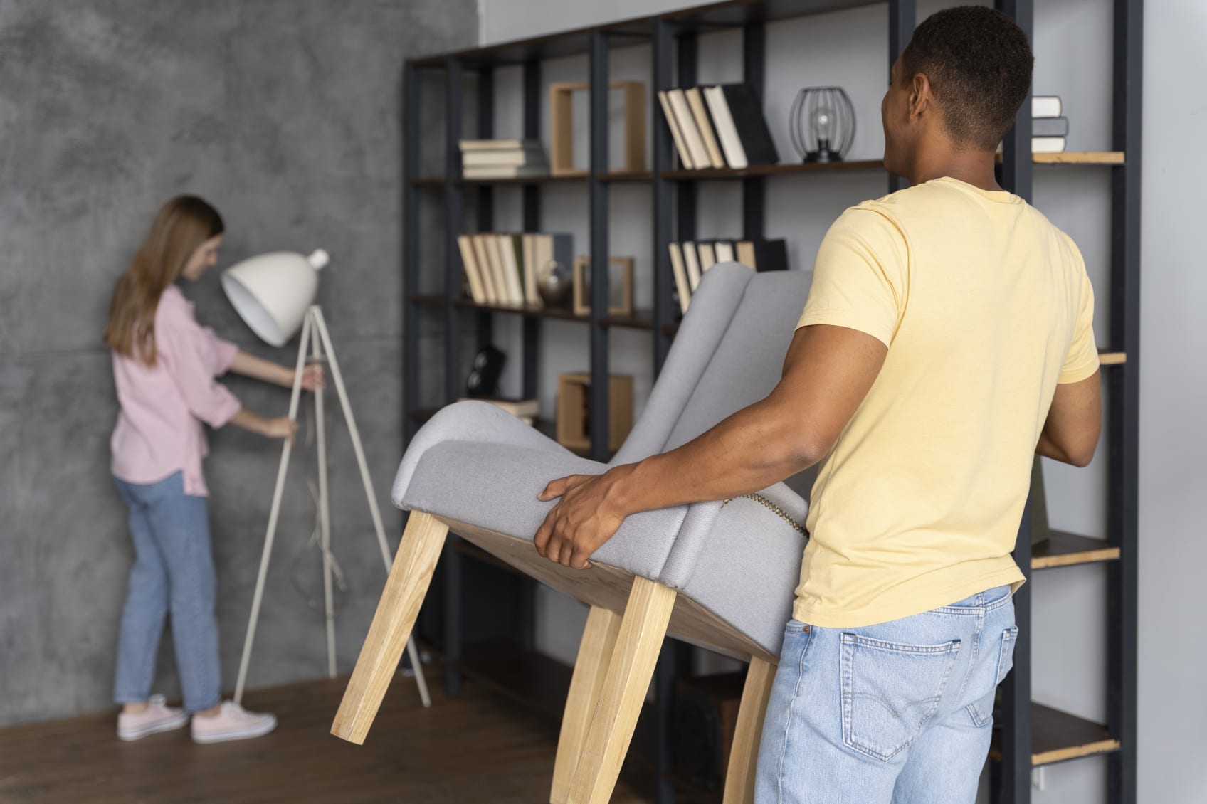 A man and woman moving furniture into a basement living area.