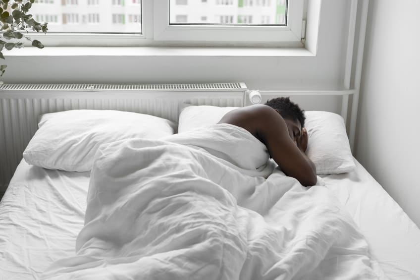 A man asleep in bed with white bedding next to a window