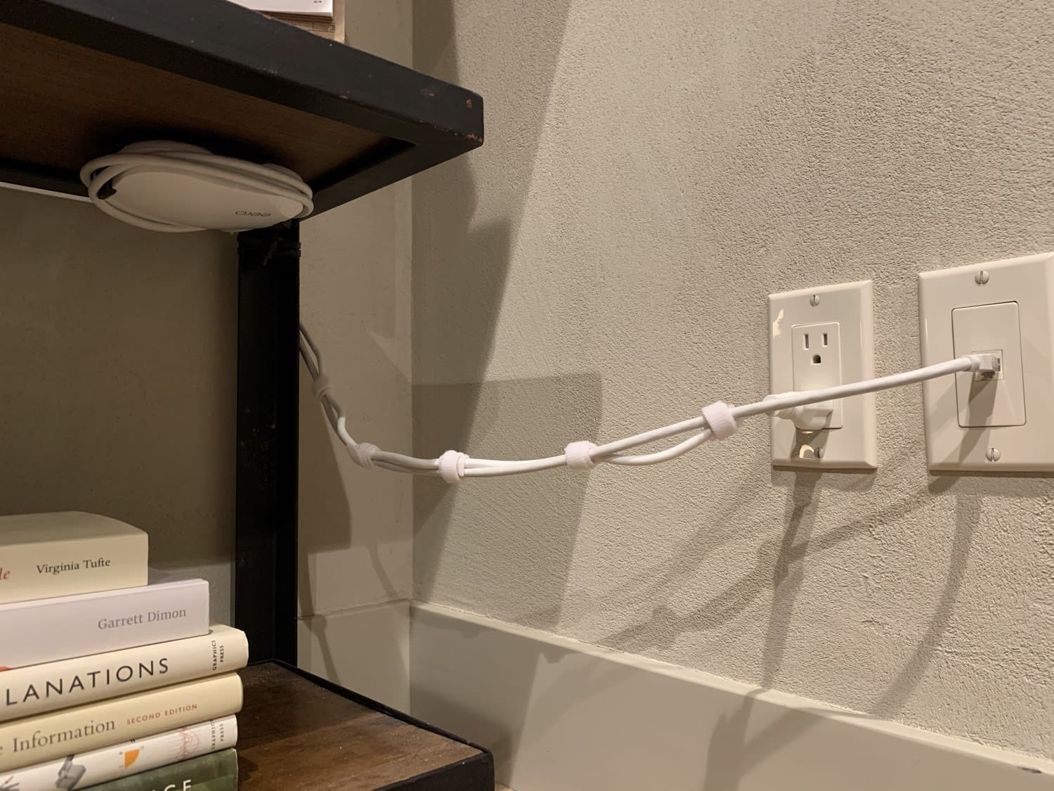A photo of a network cable and power cord to a wireless router mounted on the underside of a nearby shelf.